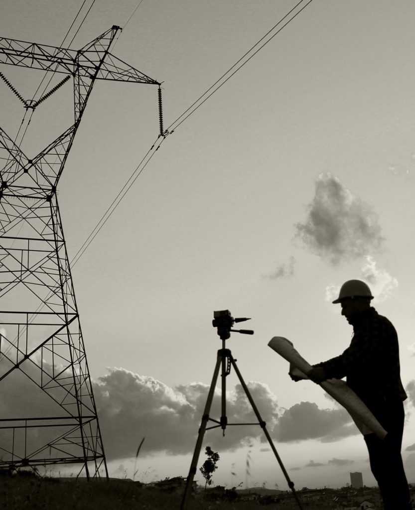 Silhouette of someone taking a land survey with electrical tower in the background