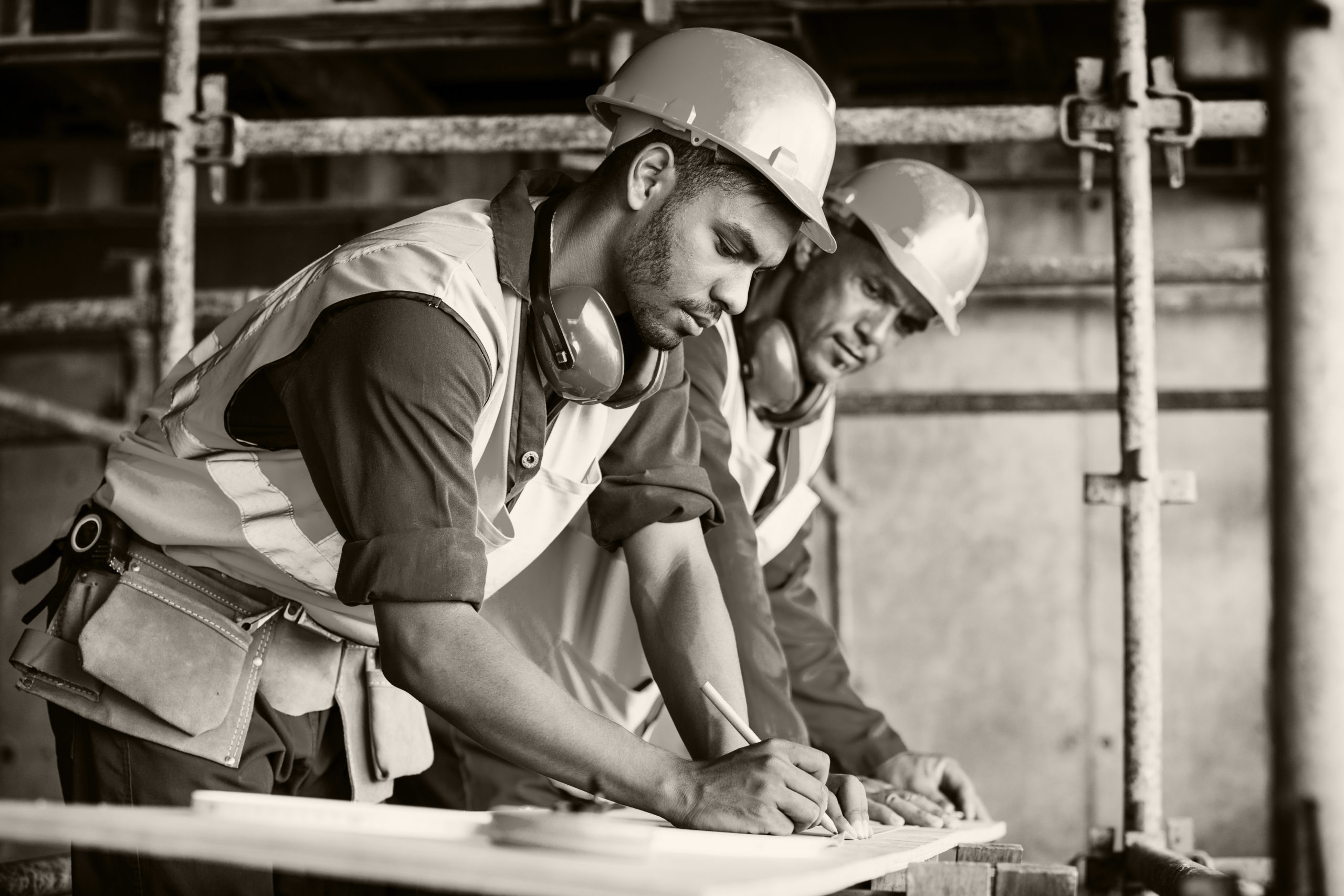 Two men in hardhats, one younger than the other, look over blueprints