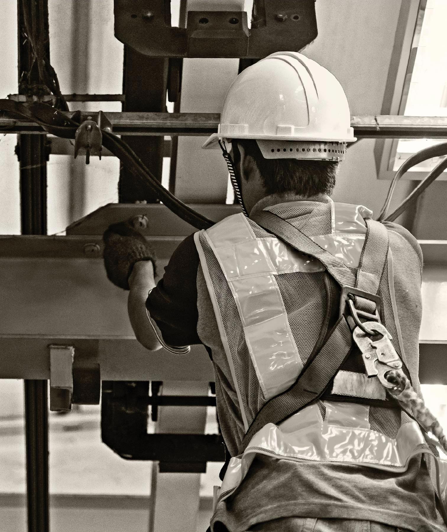 a back view of someone dress in a hard hat, harness and safety vest while handling machinery