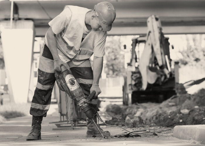 Builder worker with pneumatic hammer drill equipment breaking asphalt at road construction site
